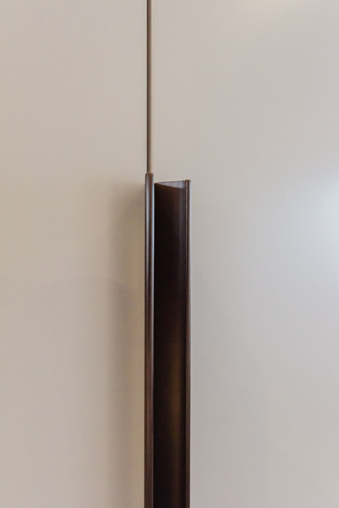 Detail van een verticale bronskleurige greeplijst tussen twee greeploze kastfronten in gebroken wit