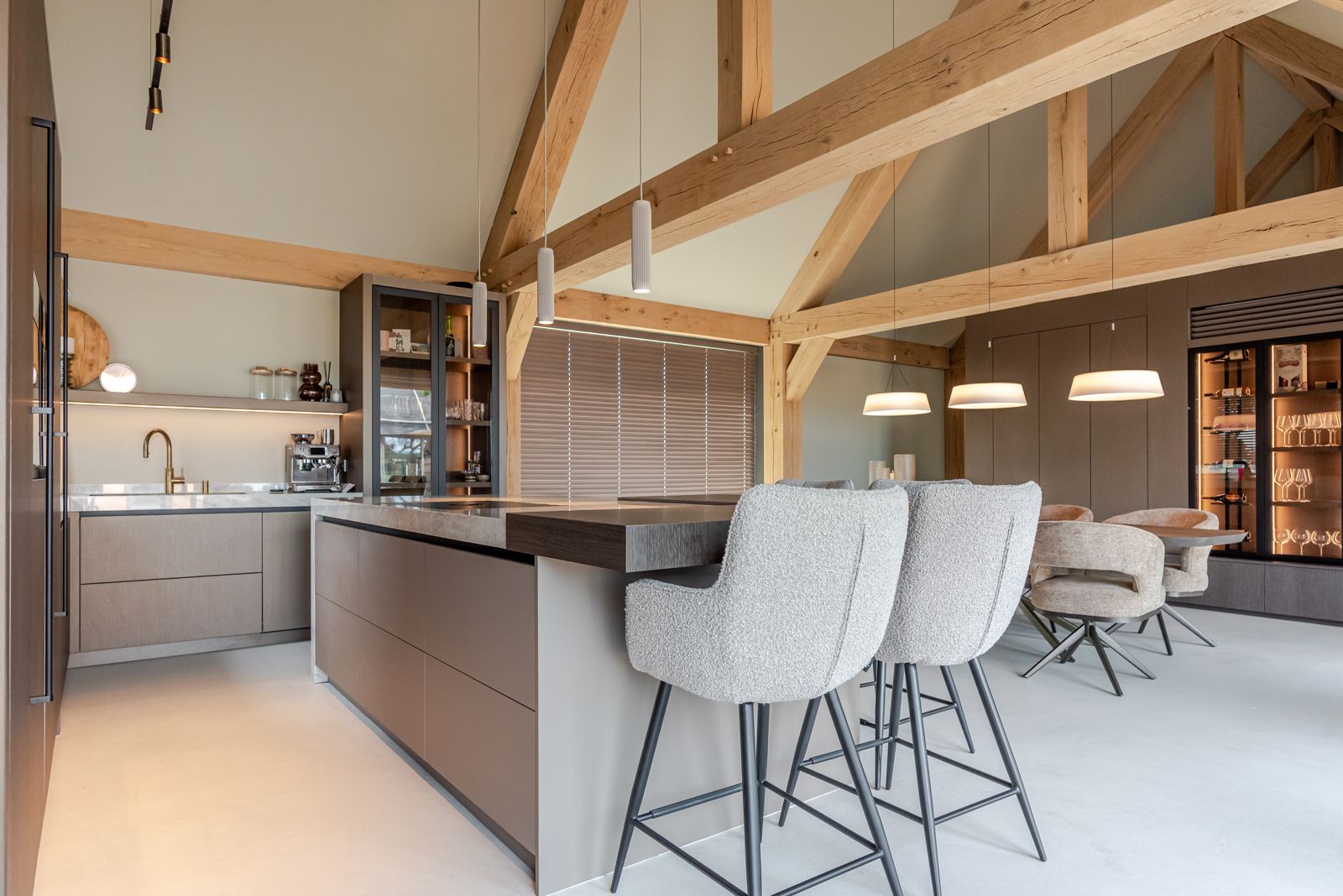 Open woonkeuken op maat met eiland en barkrukken, eethoek onder hanglampen en een verlichte wijnwand