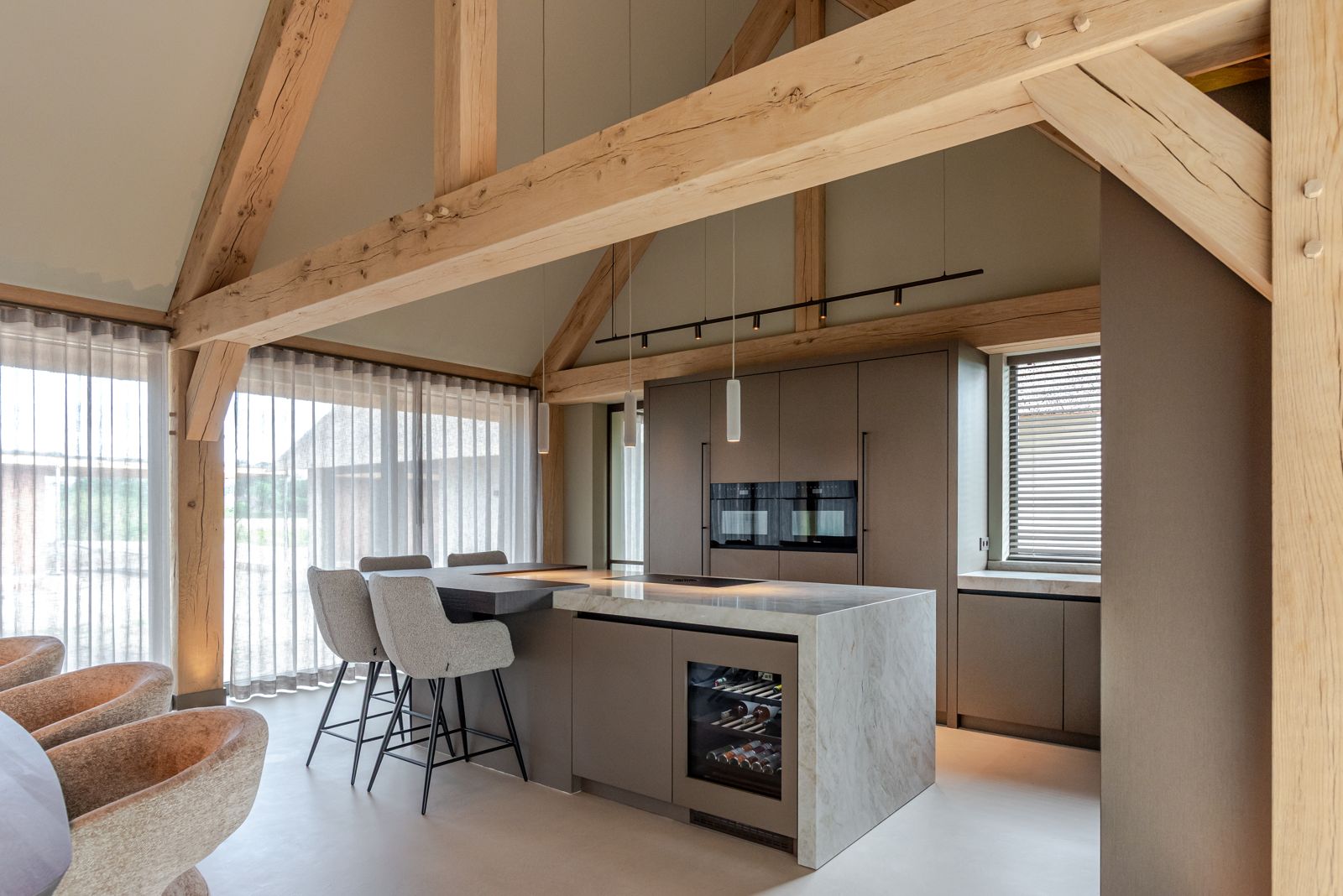 Keuken op maat met kookeiland, bardeel en ingebouwde wijnklimaatkast in een hoge ruimte met eiken spanten