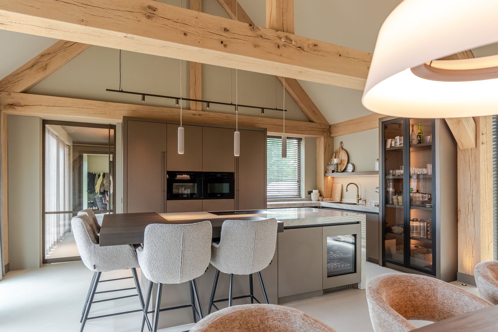 Totaal interieur op maat met keuken, kolomkasten en kookeiland met barkrukken onder eiken spanten