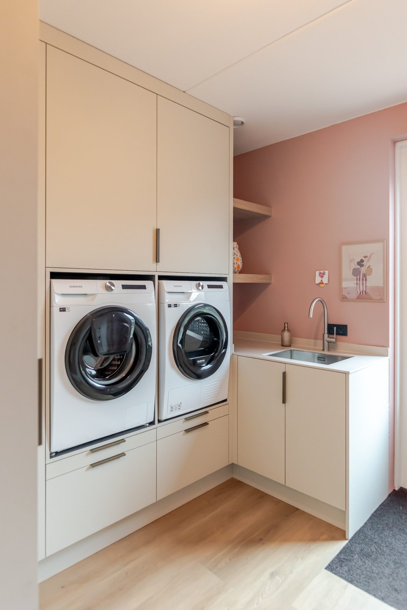 Bijkeuken op maat met zandkleurige kasten, wasmachine op hoogte en hoekopstelling met spoelbak