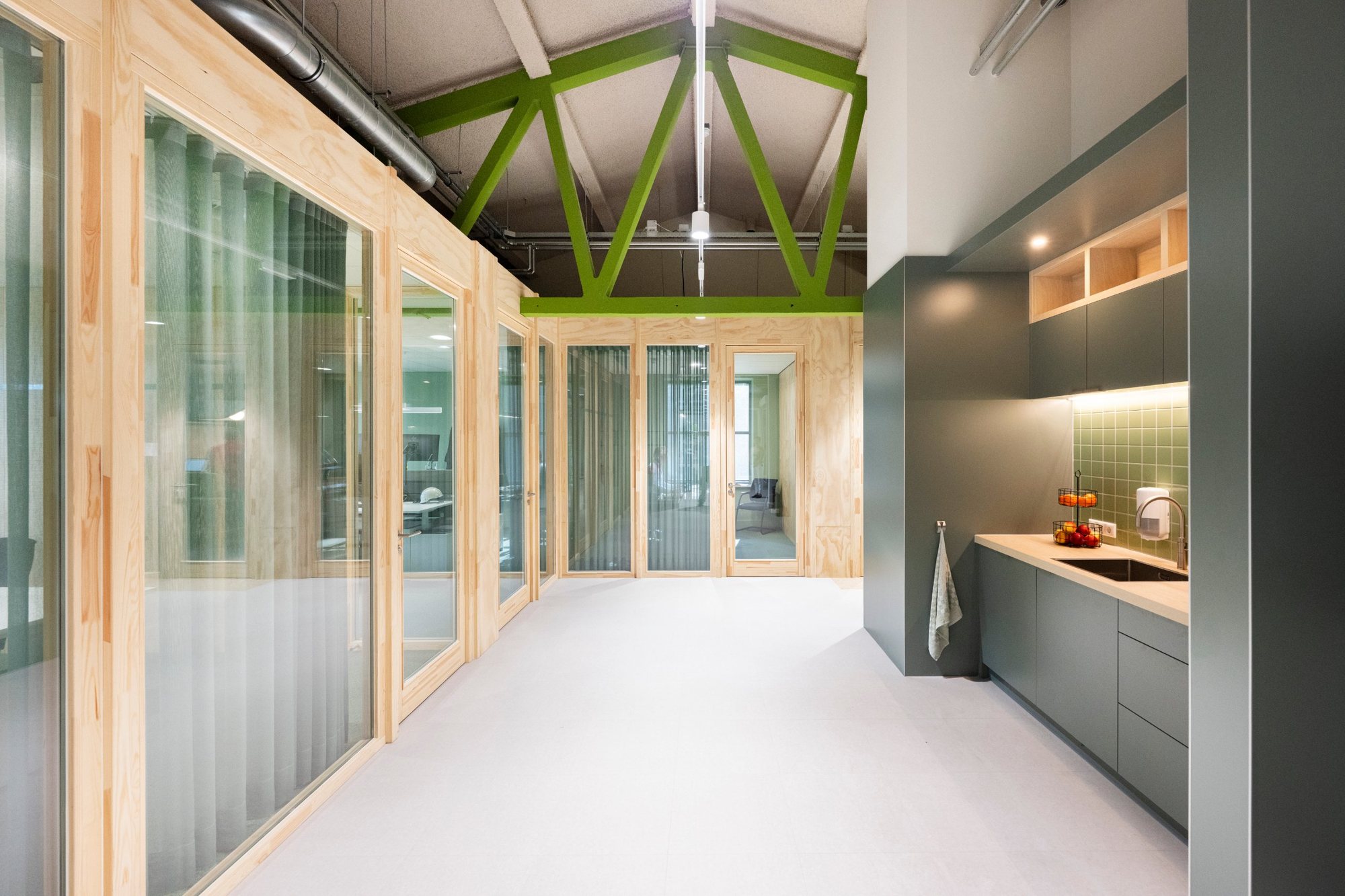 Houten kantoorwanden met glas op maat onder groene stalen spanten, met pantry op maat ernaast