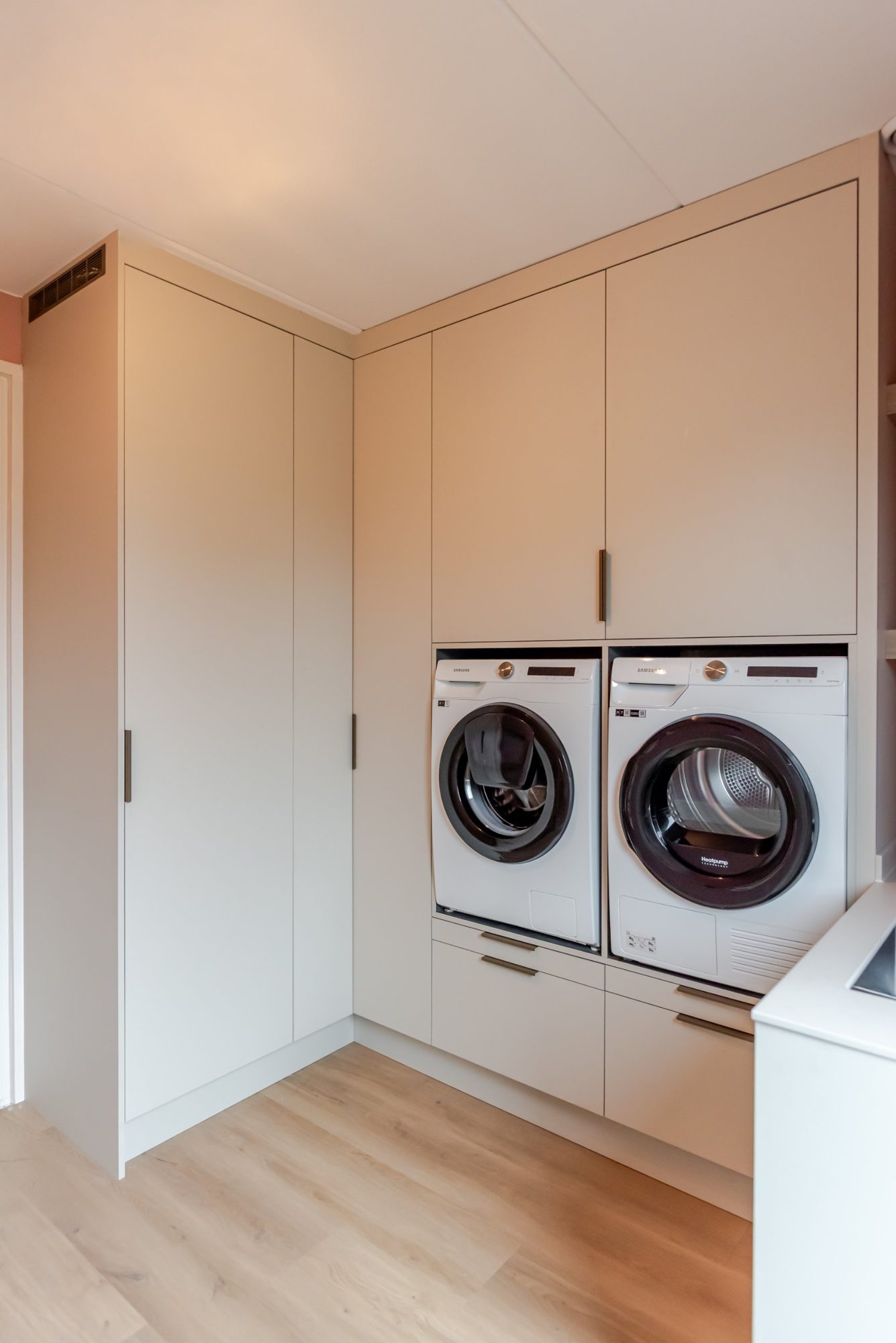 Kastenwand op maat tot het plafond in een hoek van de waskamer, met wasmachine en droger op werkhoogte