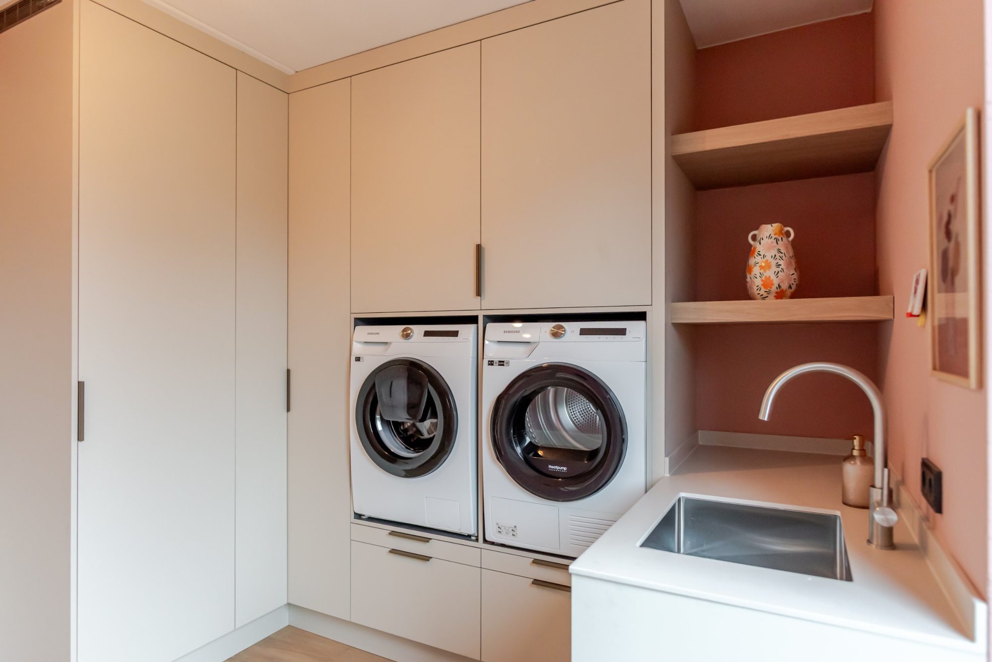 Wasruimte op maat met wasmachine en droger op hoogte, spoelbak en open eiken planken in een terracotta nis
